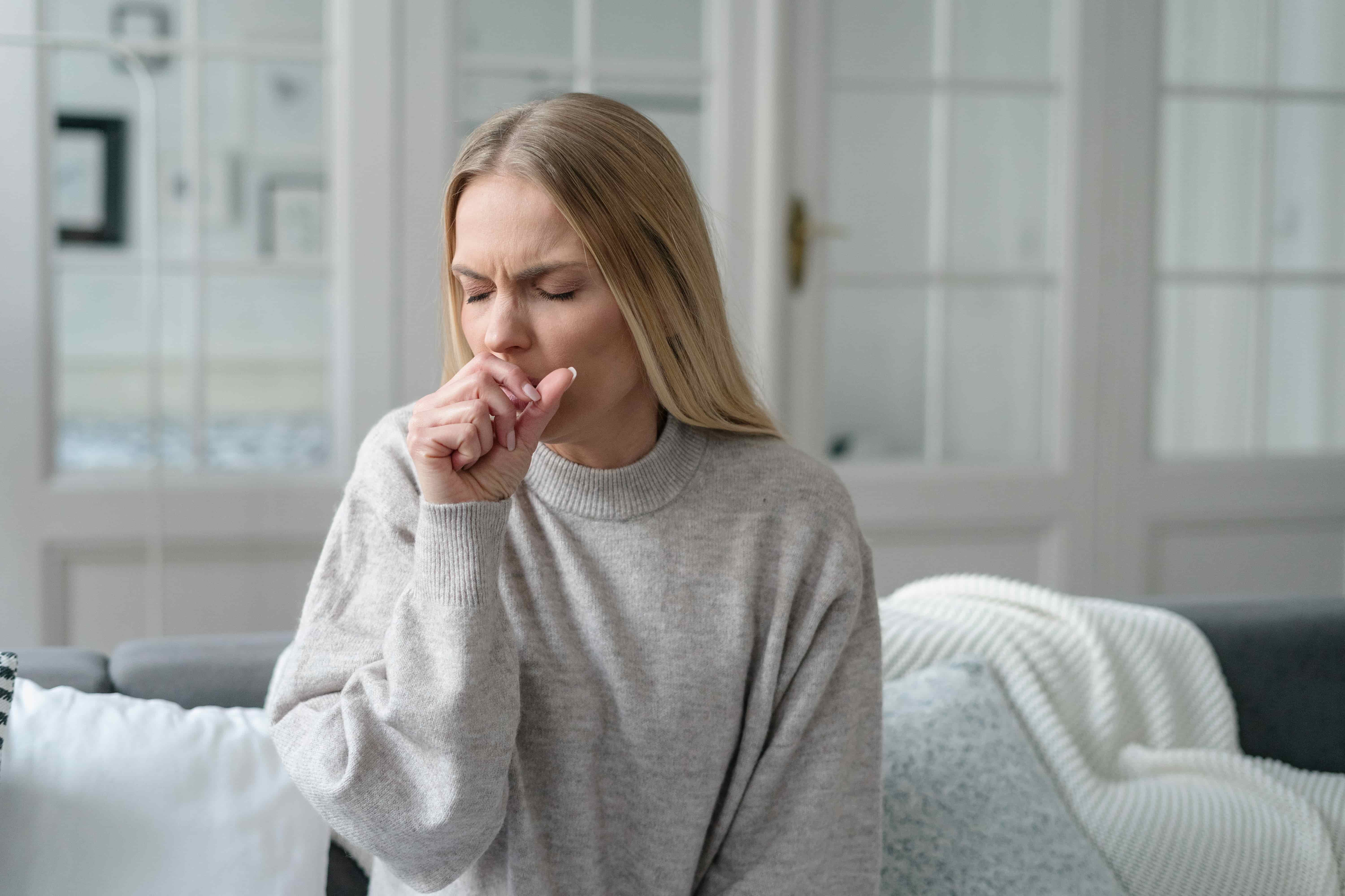Woman coughing and experiencing asthma symptoms such as shortness of breath and chest tightness