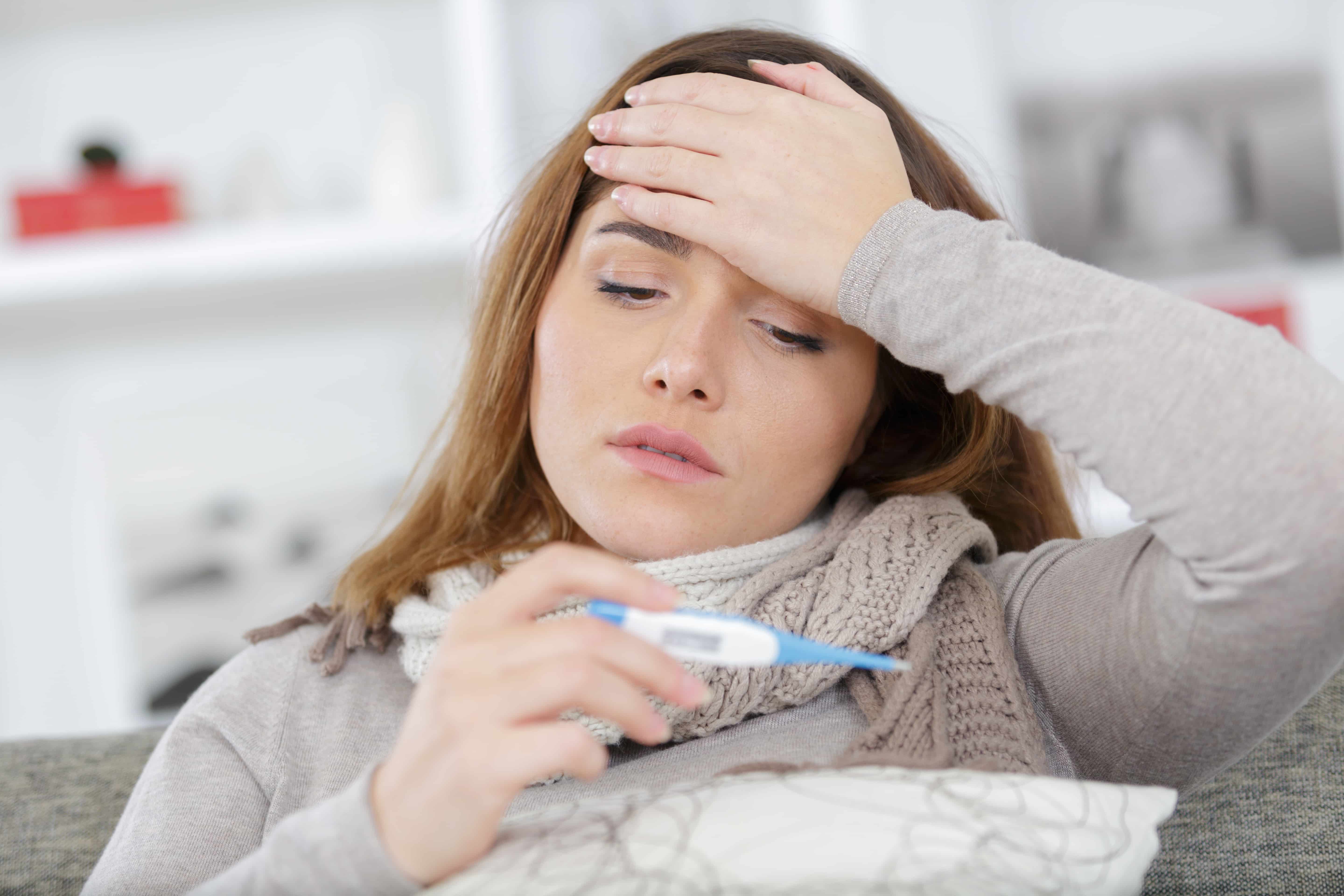 Woman checking her temperature with a thermometer showing high fever, a key symptom of strep throat