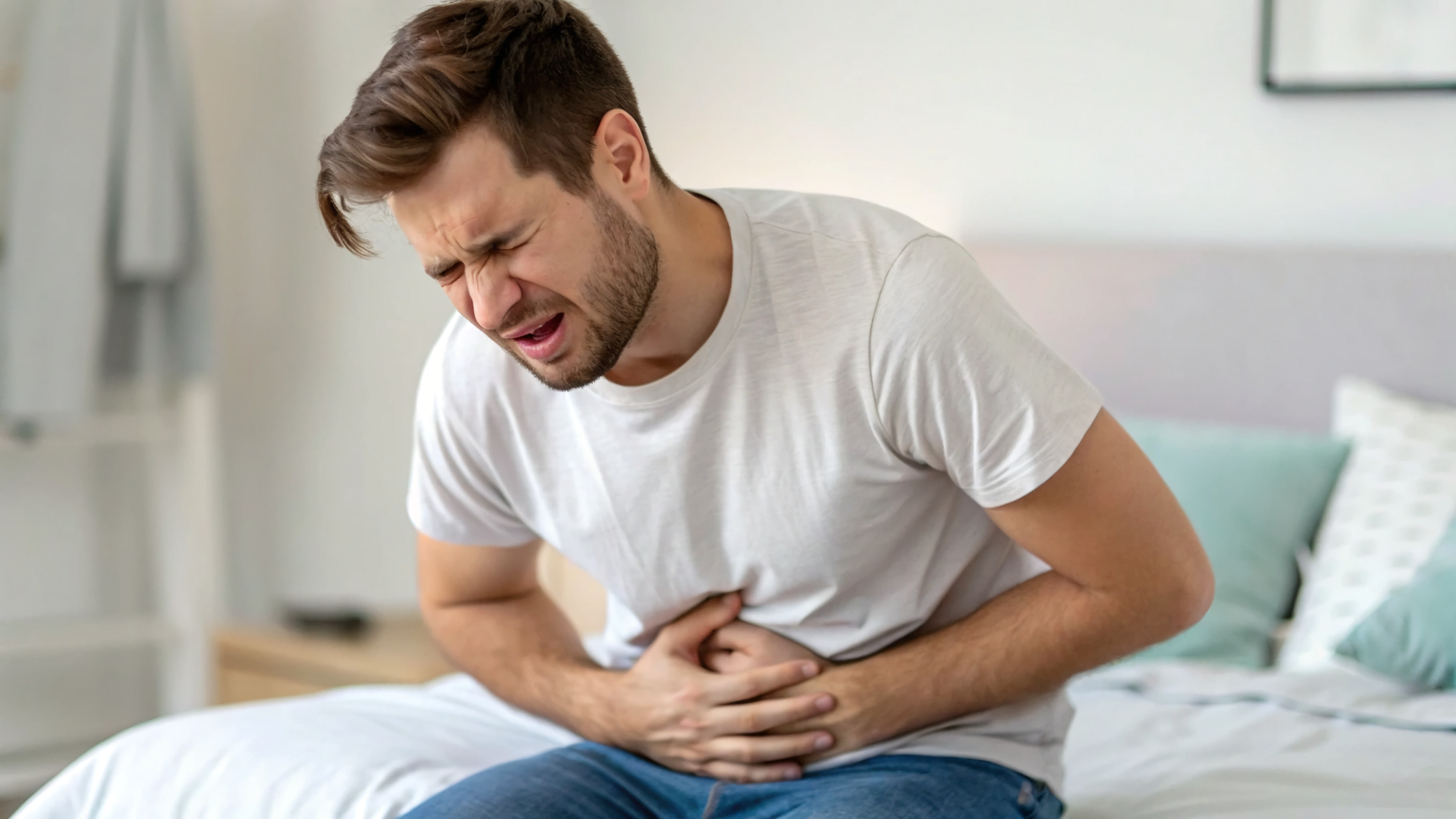 Man sitting on bed looking distressed and uncomfortable, experiencing UTI symptoms while traveling in Japan